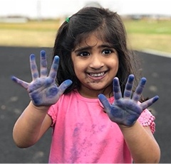 Little girl holding up hands with blue paint